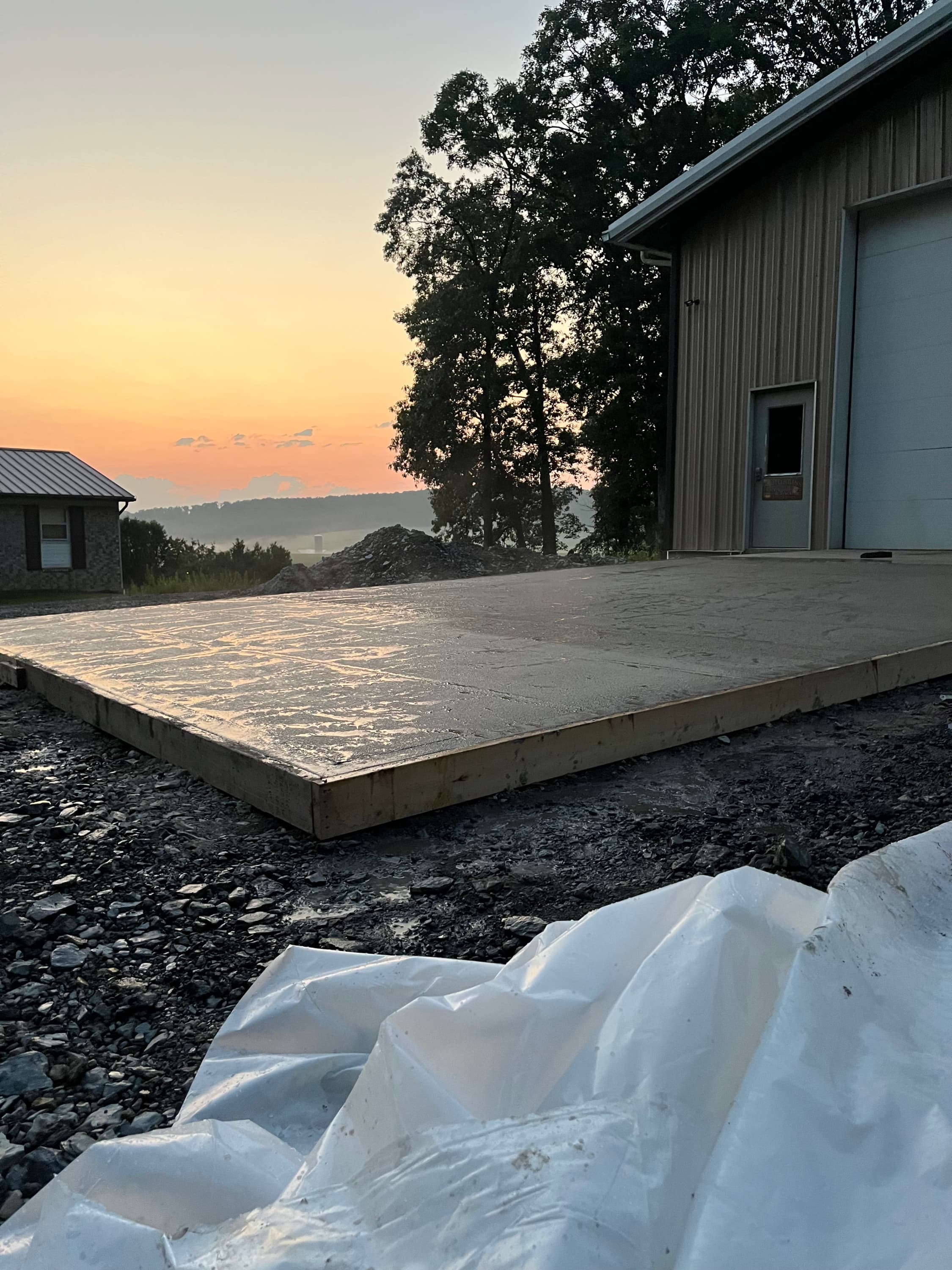 Freshly poured concrete pad in wooden forms reflecting a vibrant sunset next to a workshop.