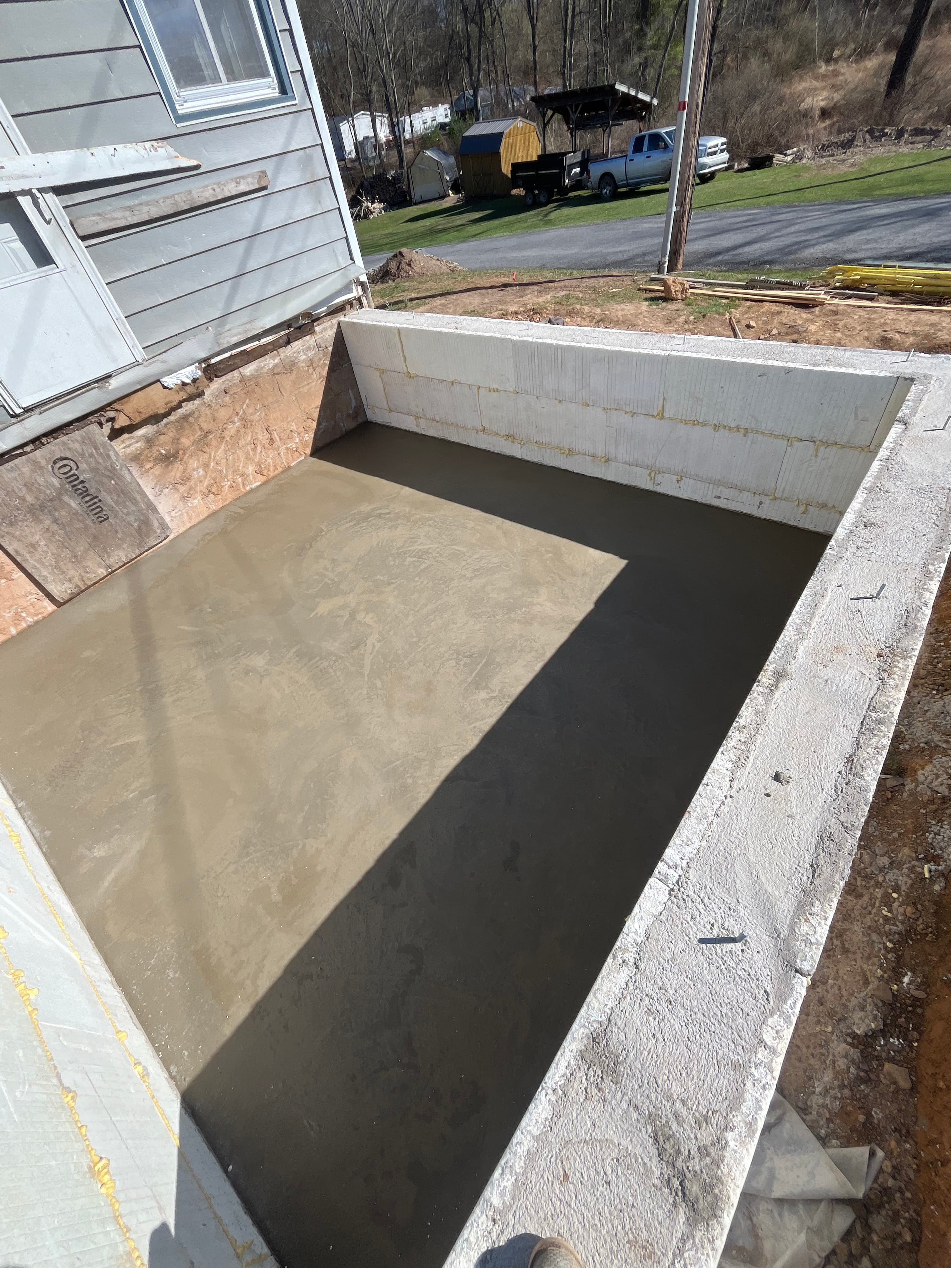 Freshly poured concrete slab inside a foundation with white insulation panels at a construction site.