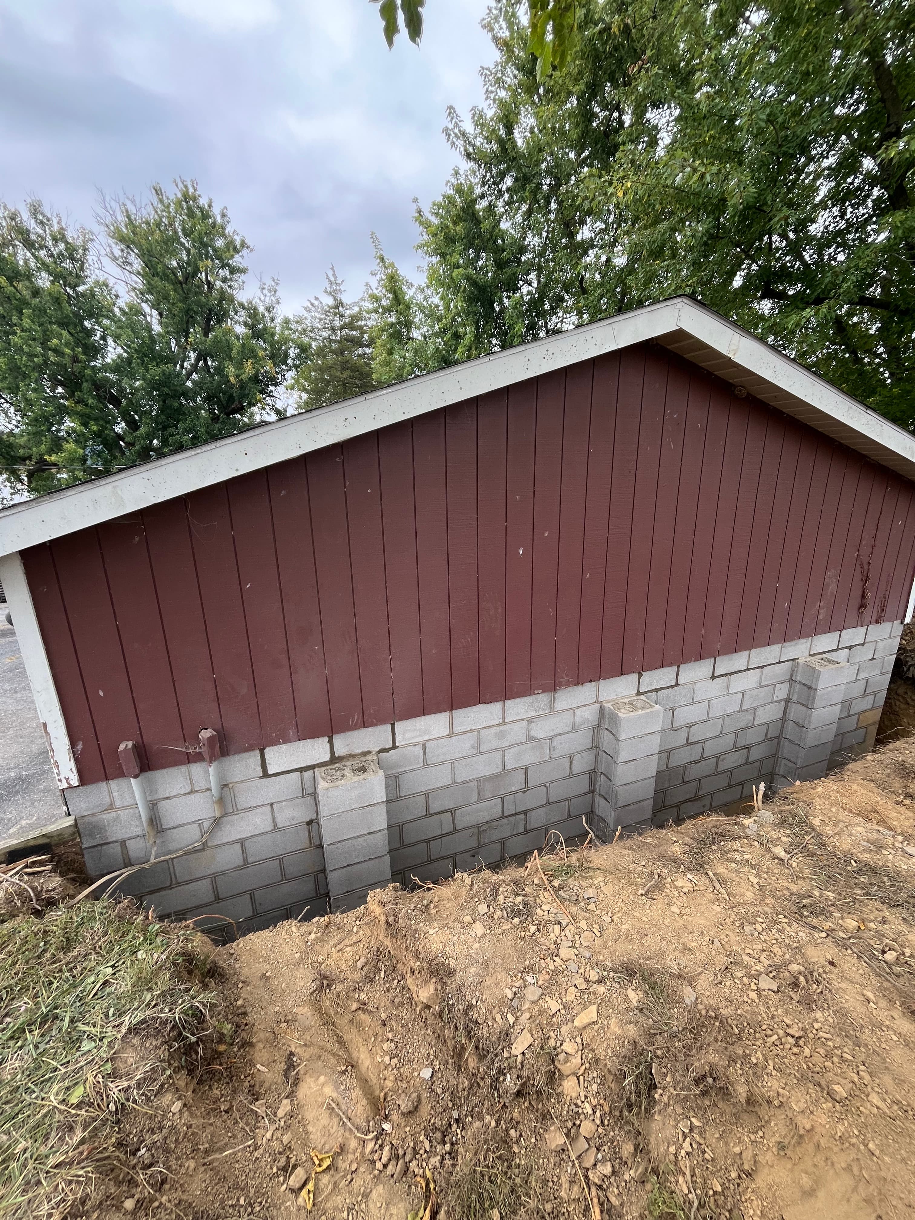 Red building with horizontal siding on a concrete block foundation next to excavated soil.